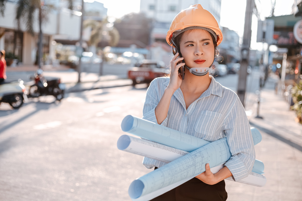 architect woman use mobile phone call with enginner or project manager between survey and checking at site construction. Architect woman hold blueprint.